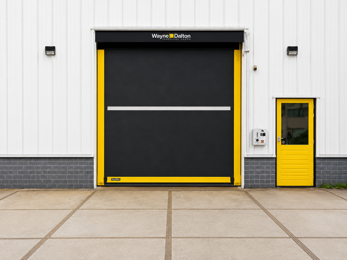 Industrial building with a large black roll-up door and a small yellow access door on a white wall
