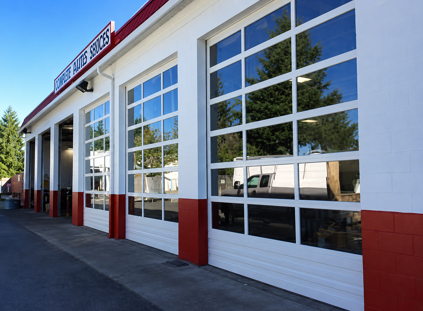 Auto repair shop exterior with white garage doors and red trim on a sunny day