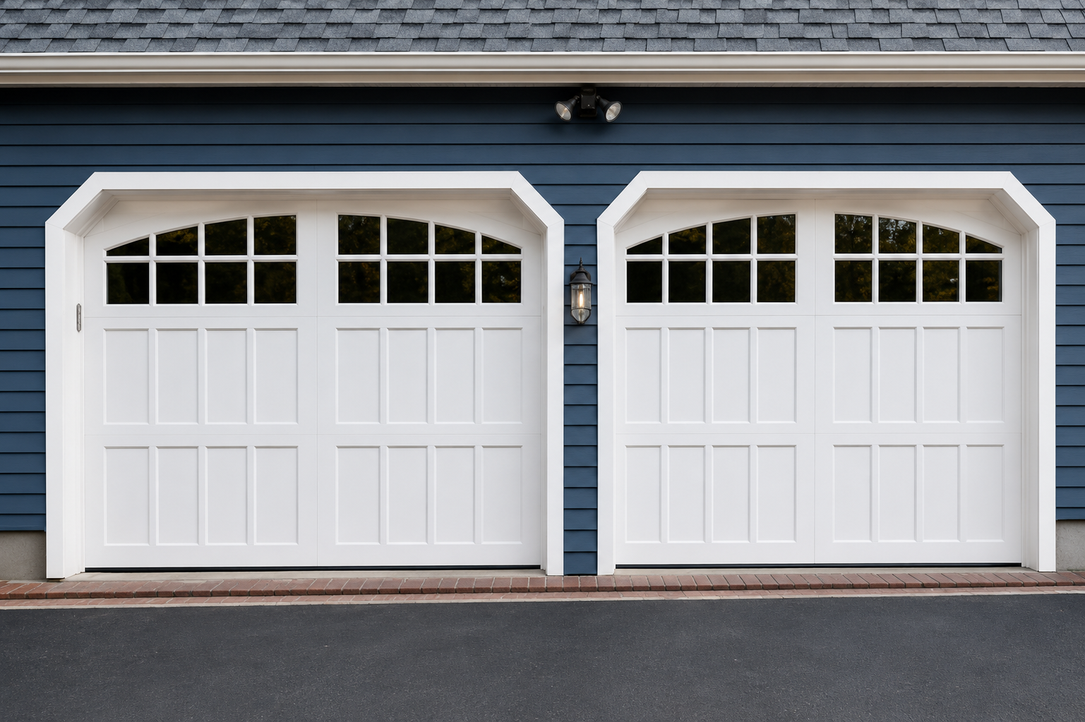 Two white garage doors with arched windows on a blue house exterior