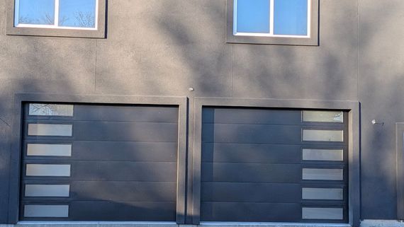 Two black garage doors on a gray building with small windows above them