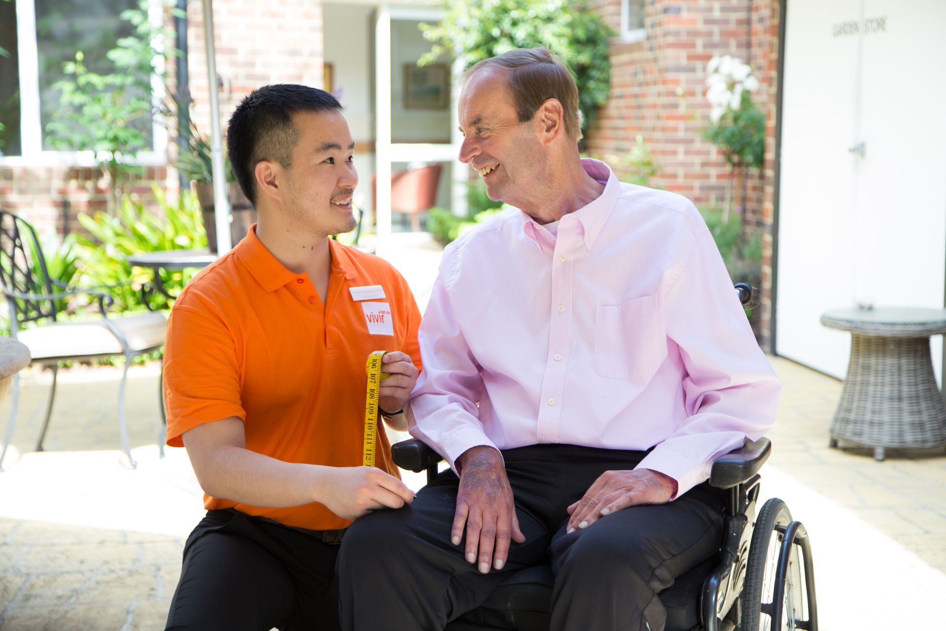 A man in an orange shirt is sitting next to a man in a wheelchair.