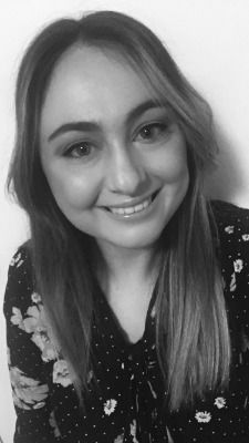 A black and white photo of a smiling woman wearing a polka dot shirt.