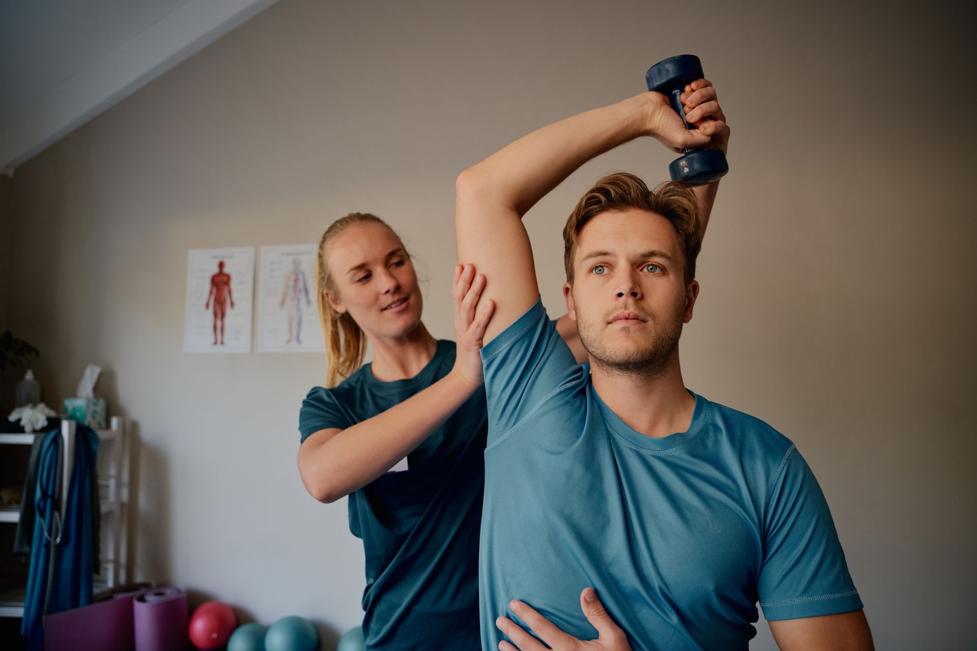 A woman is helping a man stretch his arm while holding a dumbbell.