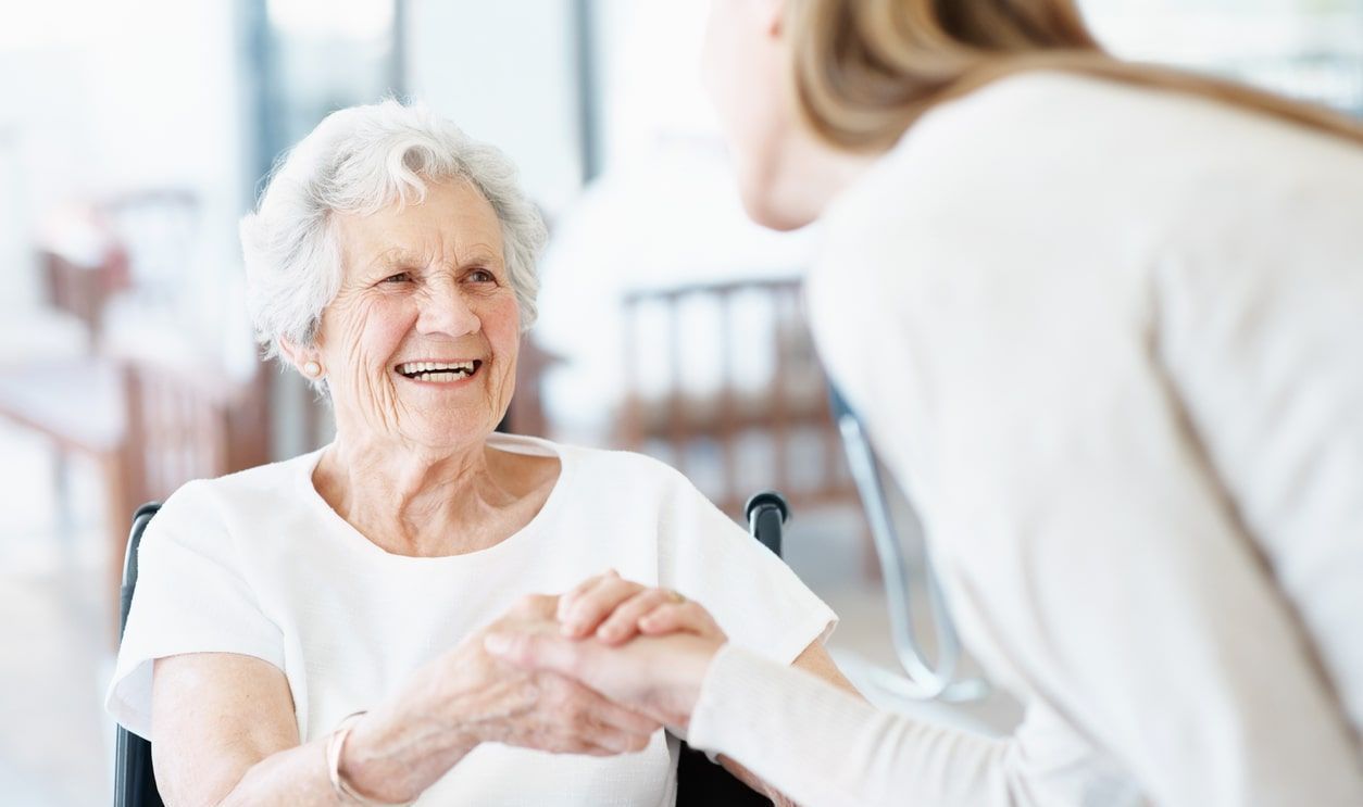 A woman is holding the hand of an elderly woman in a wheelchair.