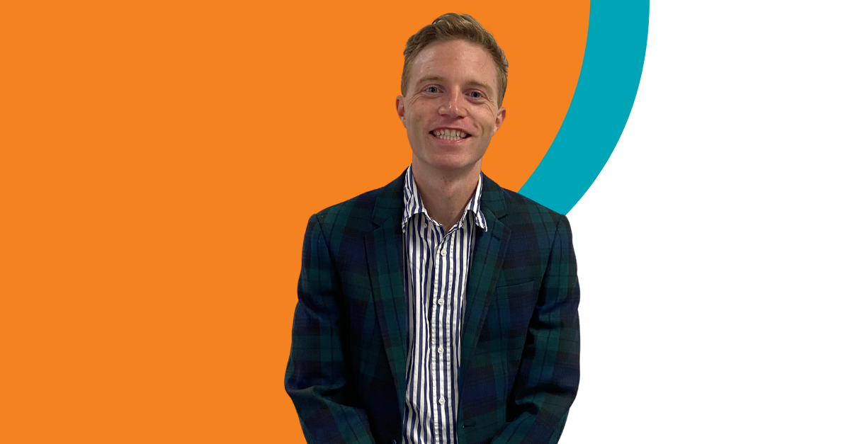 A man in a suit and striped shirt is smiling in front of an orange and blue circle.