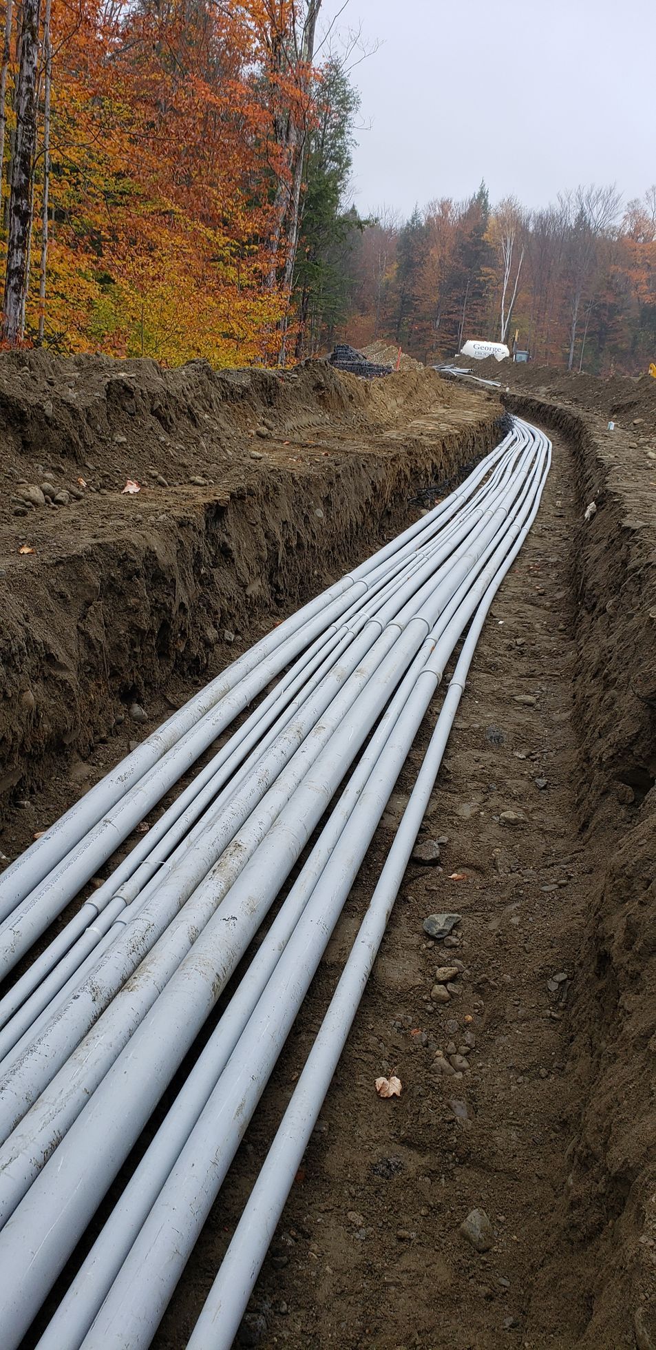 A bunch of pipes are laying in the dirt in a trench.