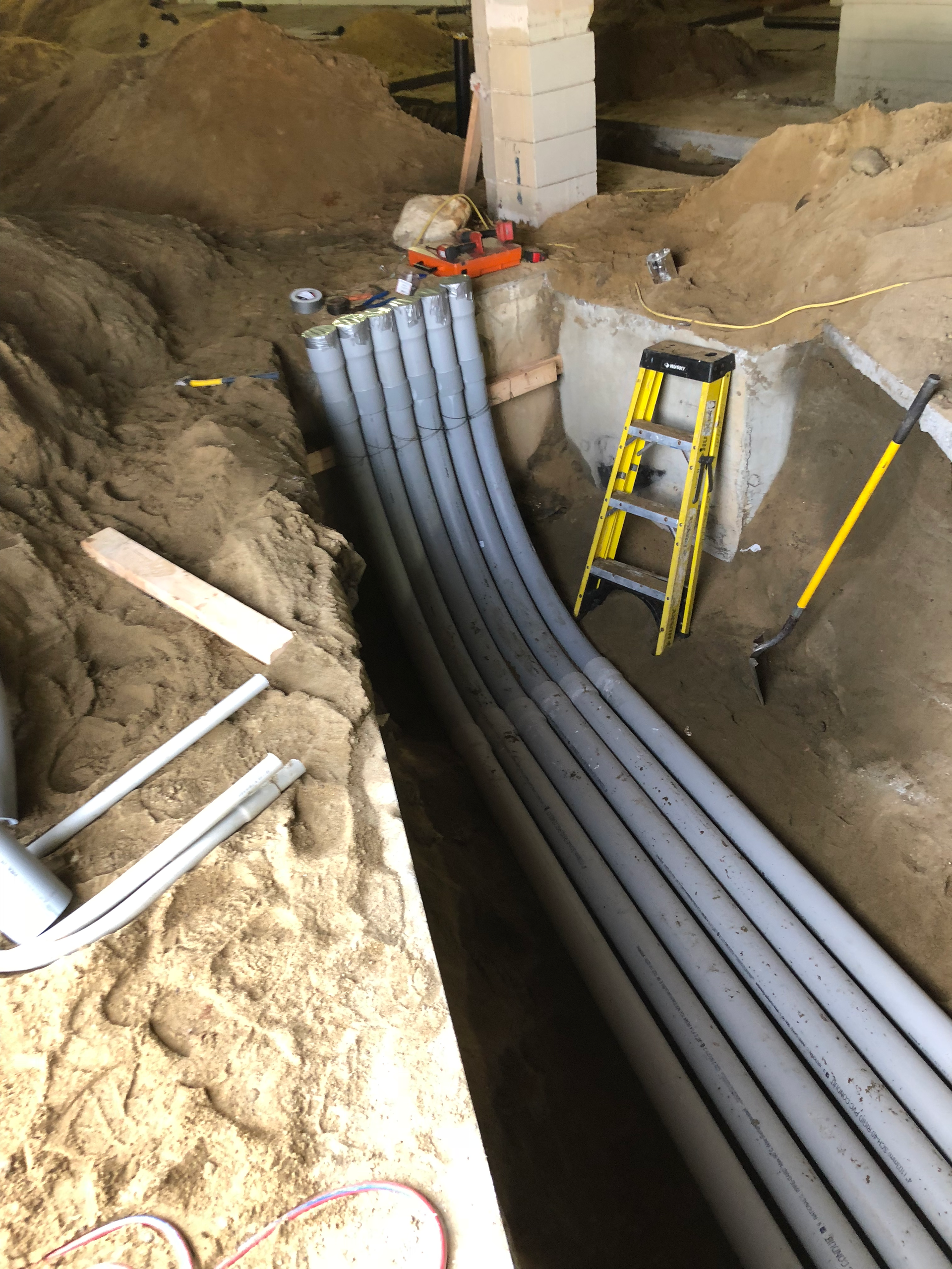 A ladder is sitting in the dirt next to a bunch of pipes