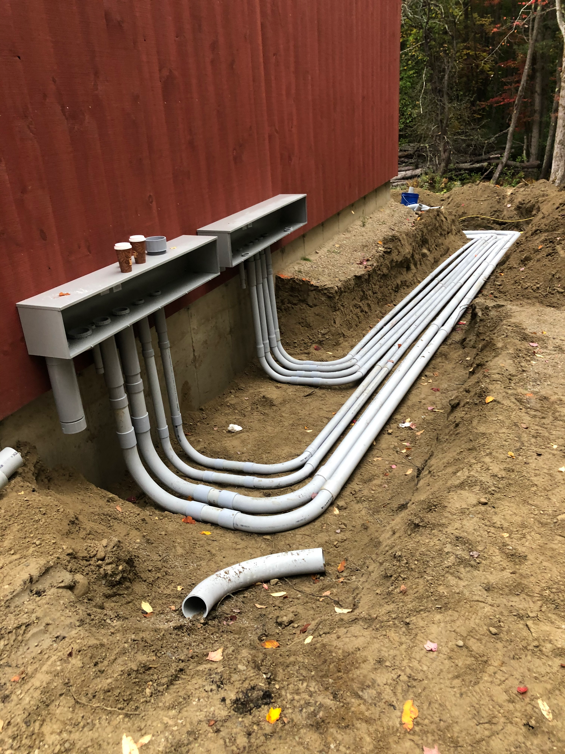 A bunch of pipes or electrical work are laying in the dirt in front of a building.