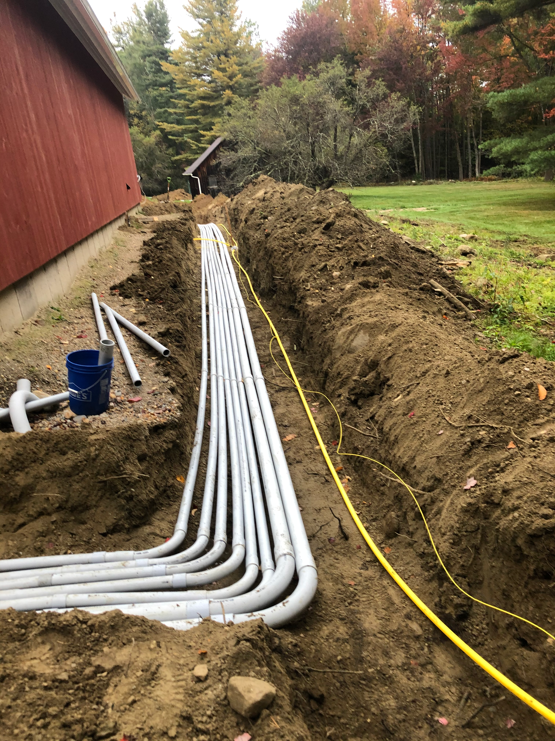 A bunch of pipes for underground electrical are laying in the dirt next to a house.