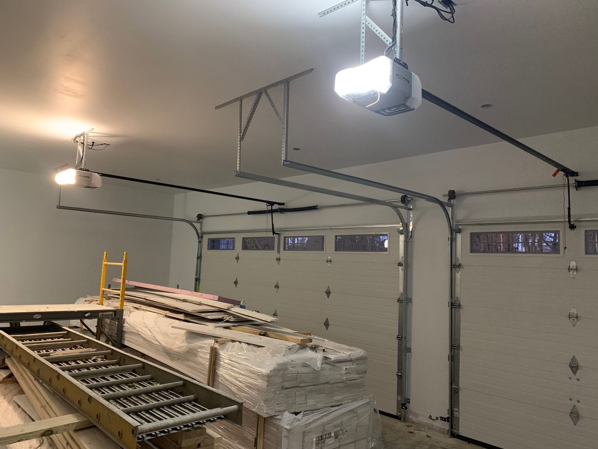 Garage interior with two open garage doors, a yellow ladder, and stacked boards on a workbench