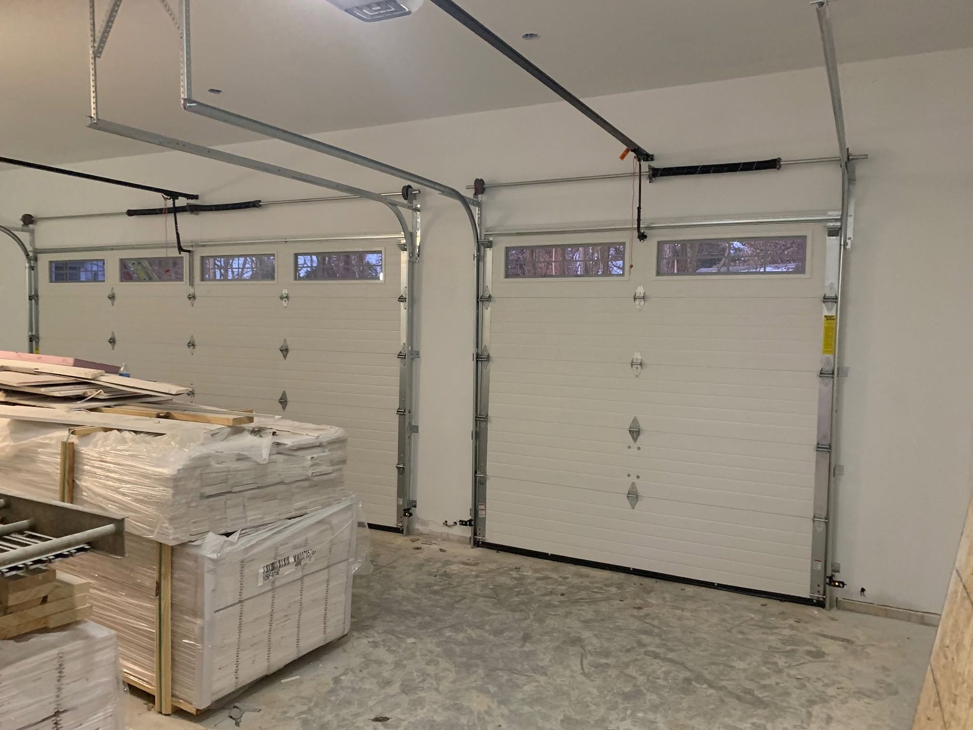 Garage interior with a closed white overhead door, stacked materials, and ceiling tracks for a door opener