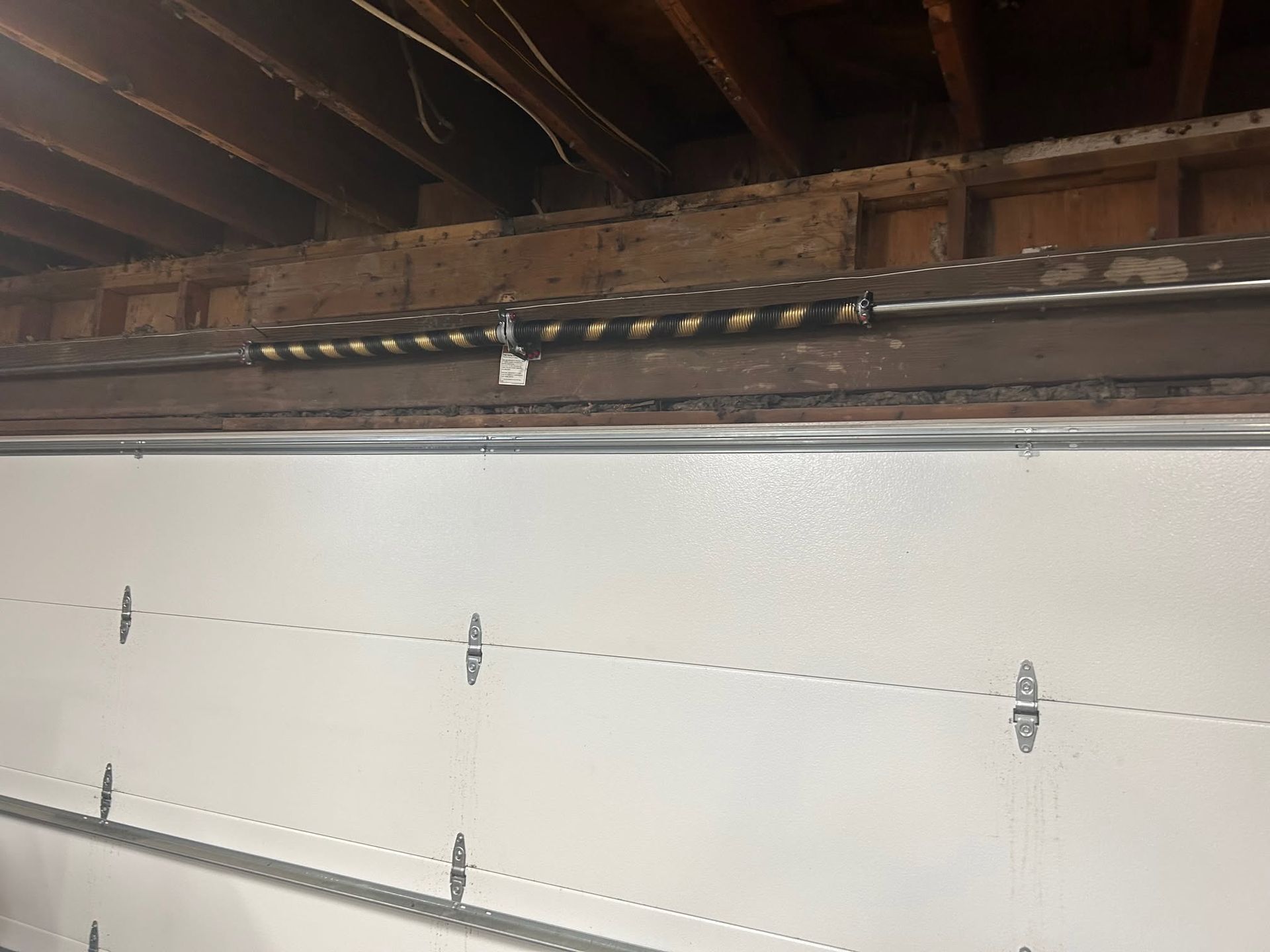 Interior garage door under exposed wooden beams with a white panel and visible wall anchors