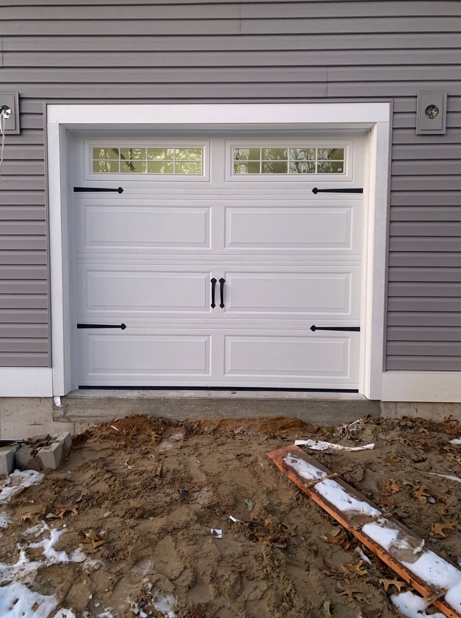 White garage door on a gray house exterior with muddy ground in front