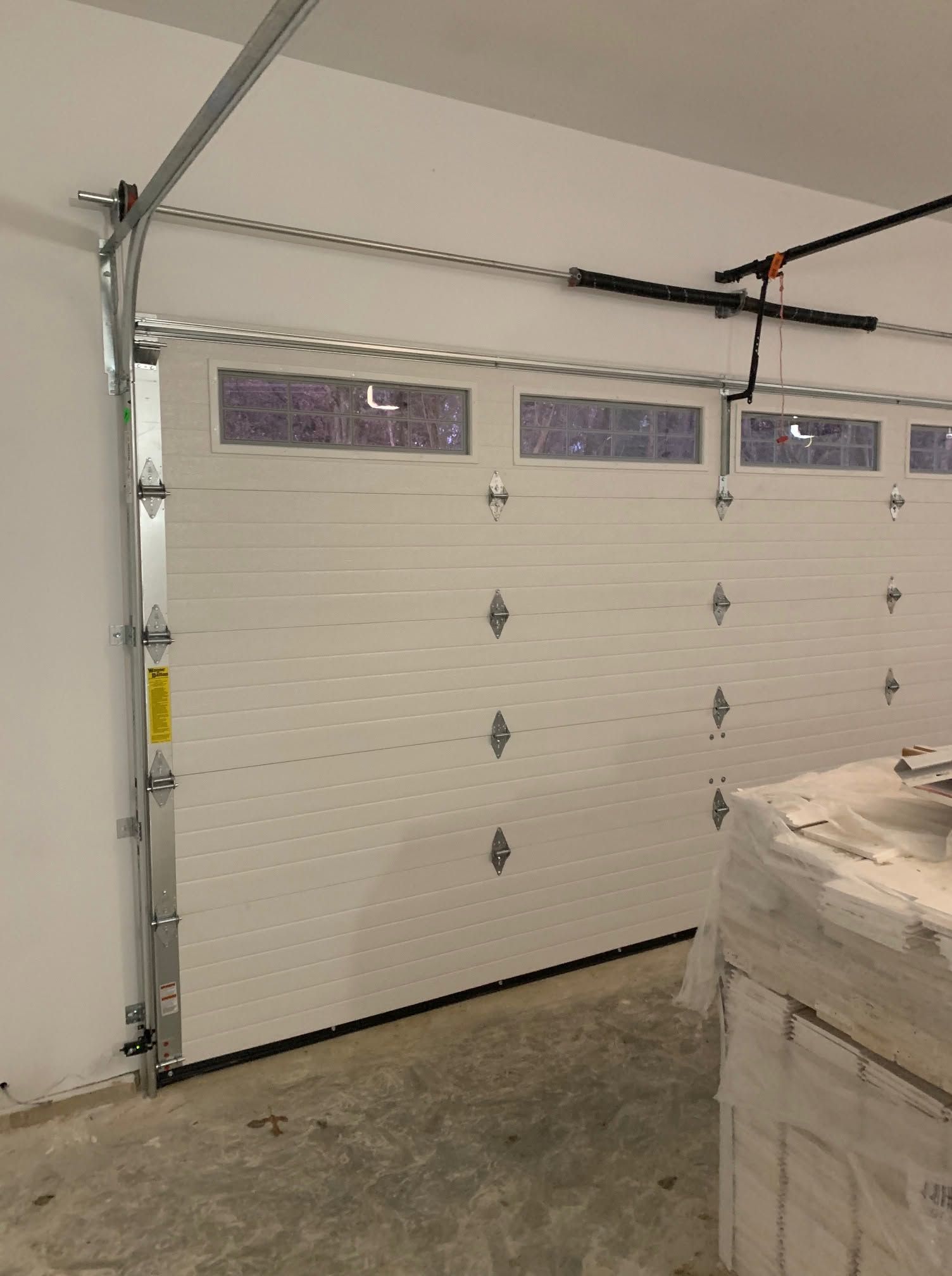 White sectional garage door inside a garage, with small windows and stacked boxes nearby.