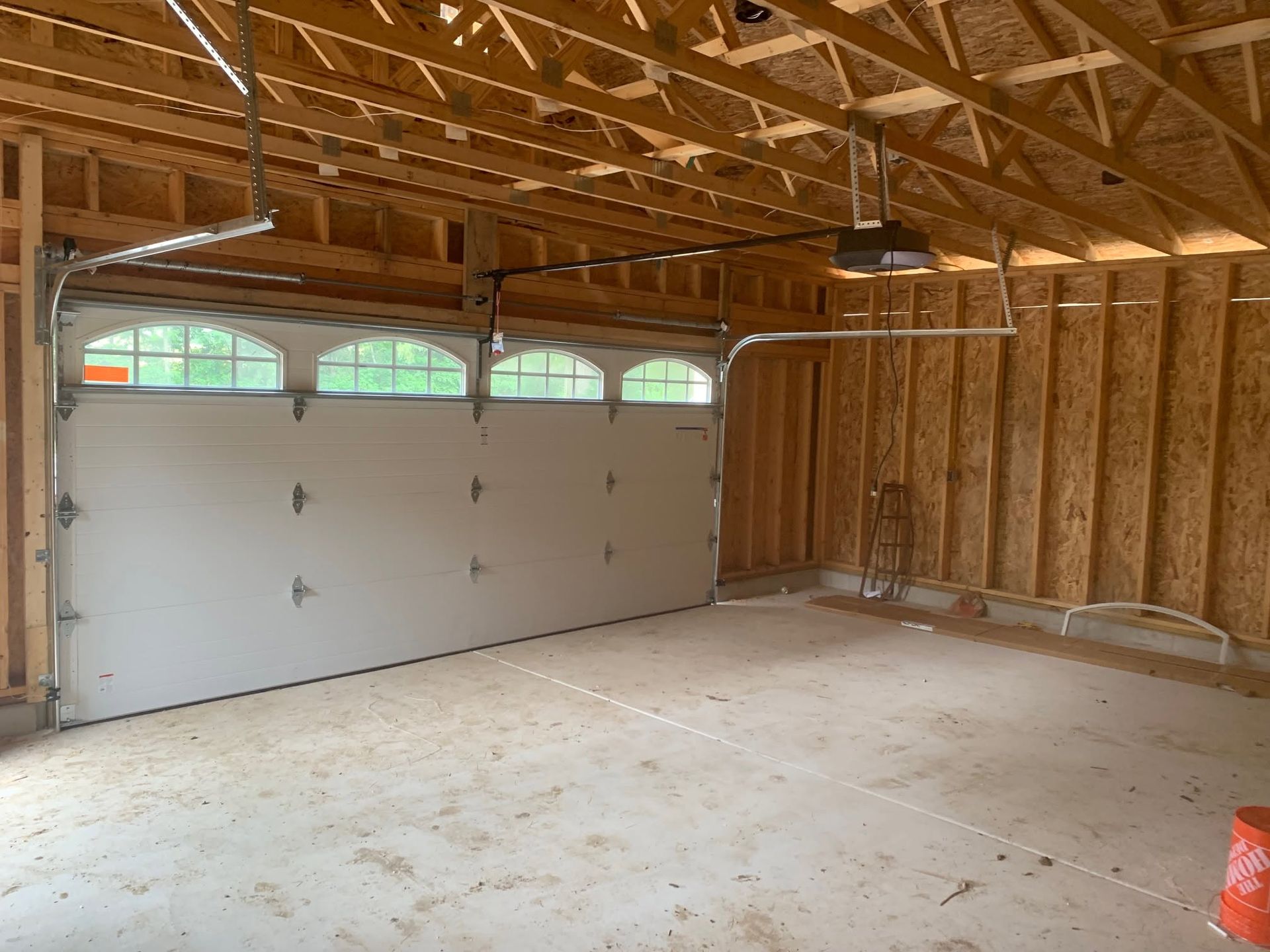 Empty unfinished garage interior with exposed wood framing and a closed white sectional door.