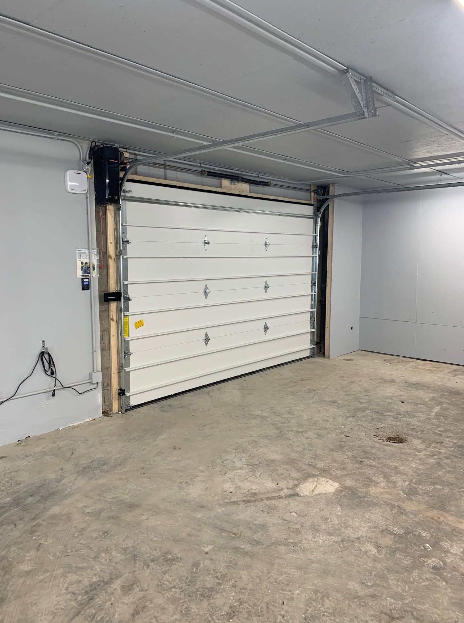 Empty garage with white sectional door, concrete floor, and exposed ceiling panels.
