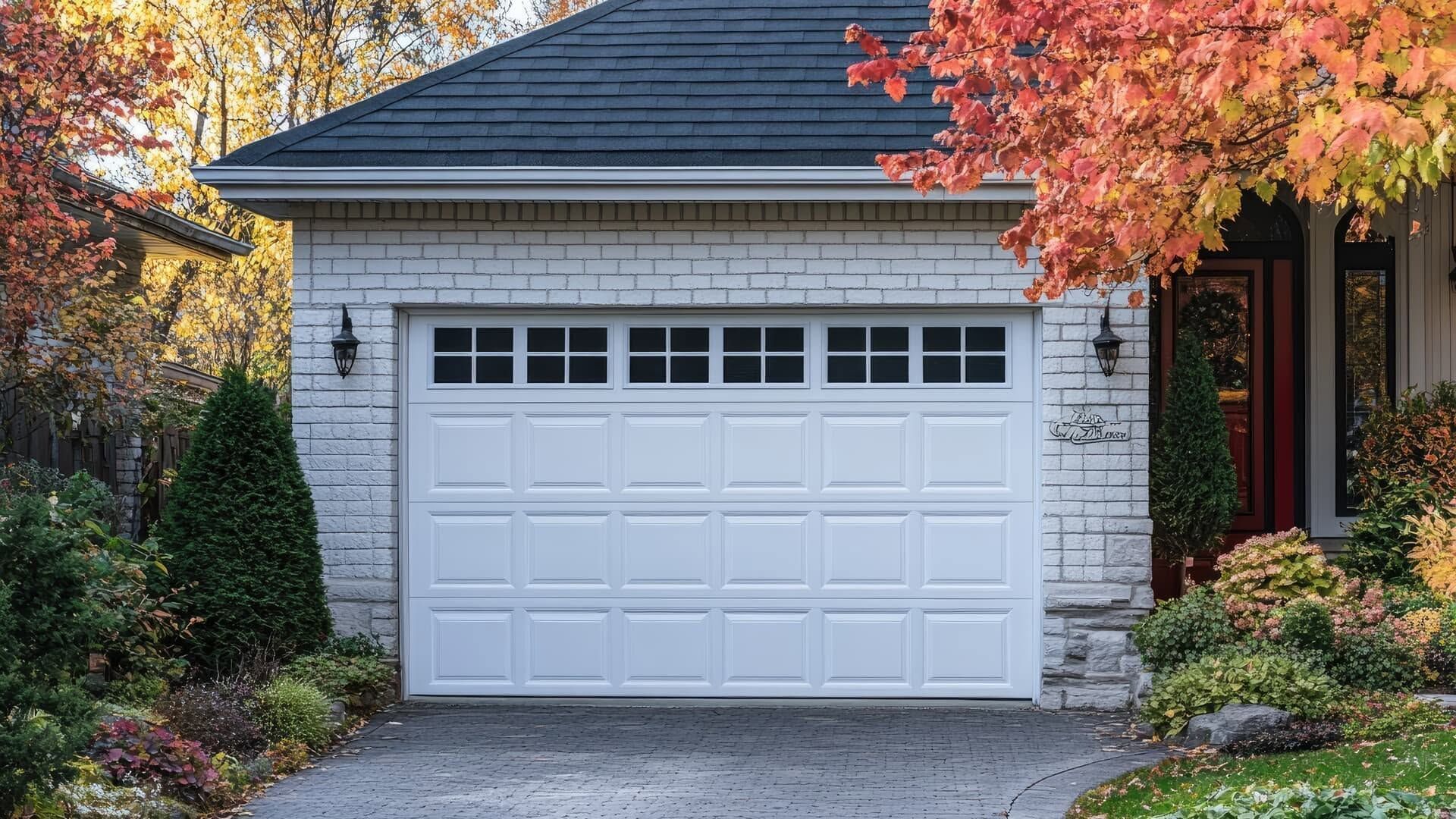 Suburban home with a white garage door framed by autumn foliage and a stone driveway.