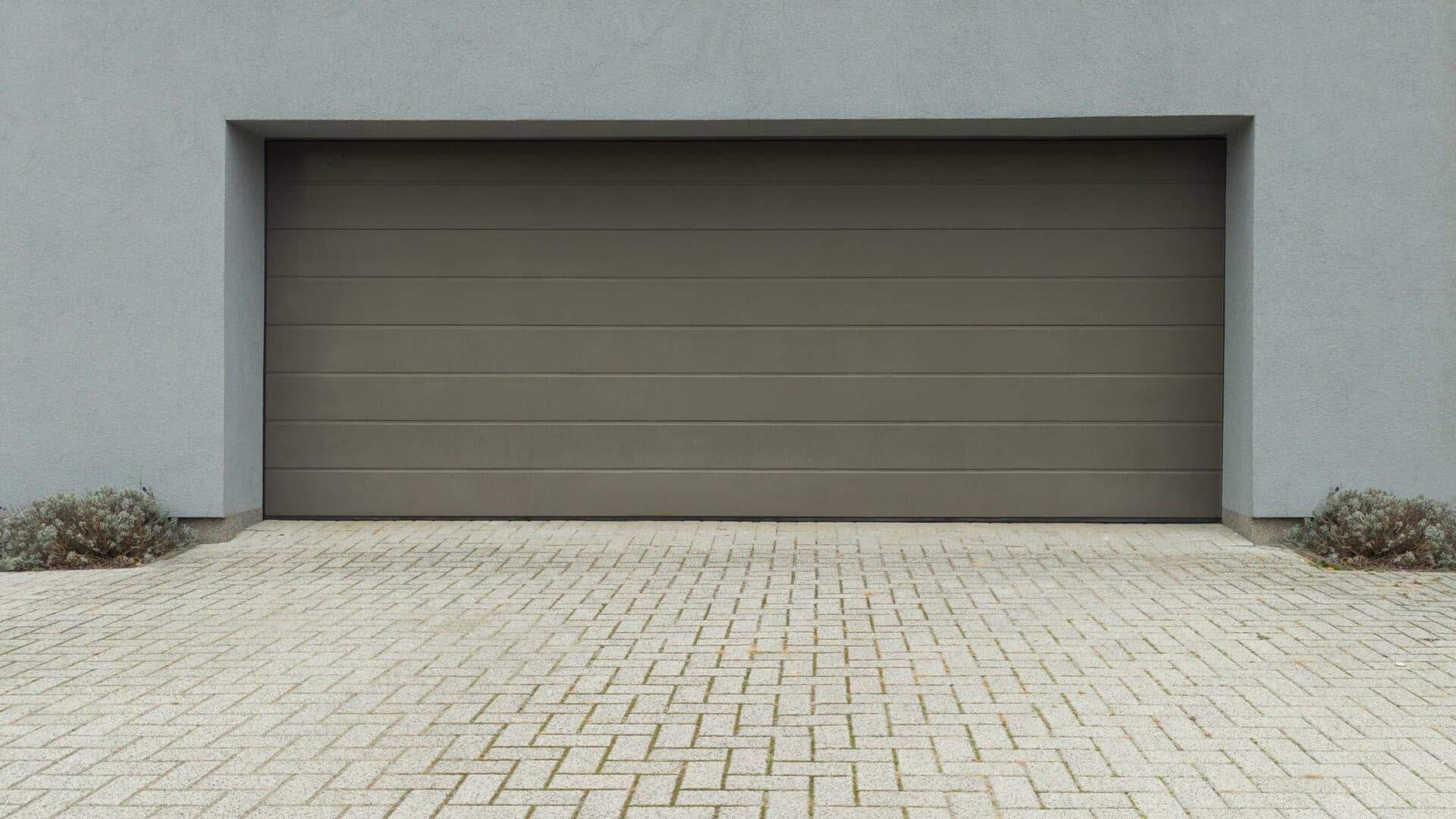 Closed brown garage door set in a gray wall above a light brick driveway