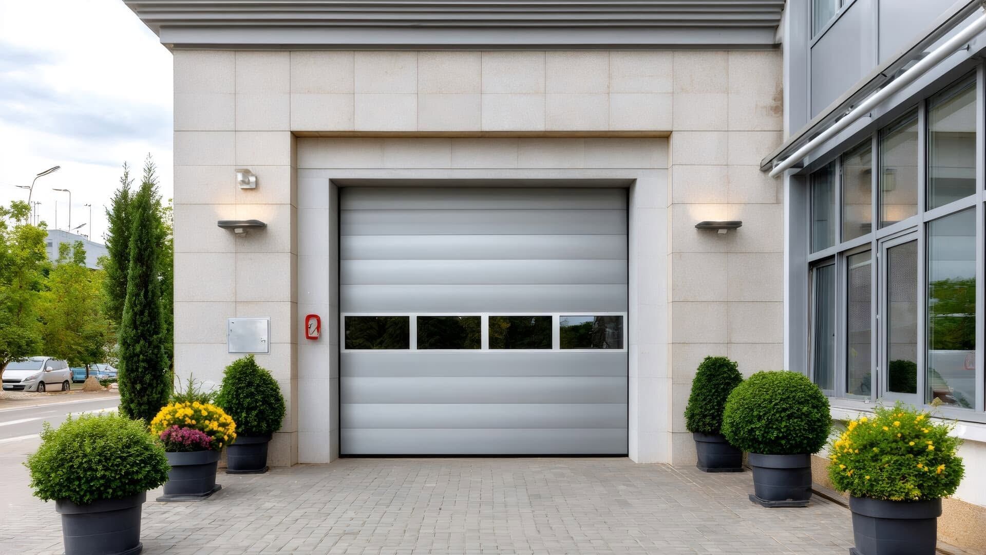 Modern building entrance with a closed white garage-style door and potted shrubs on both sides