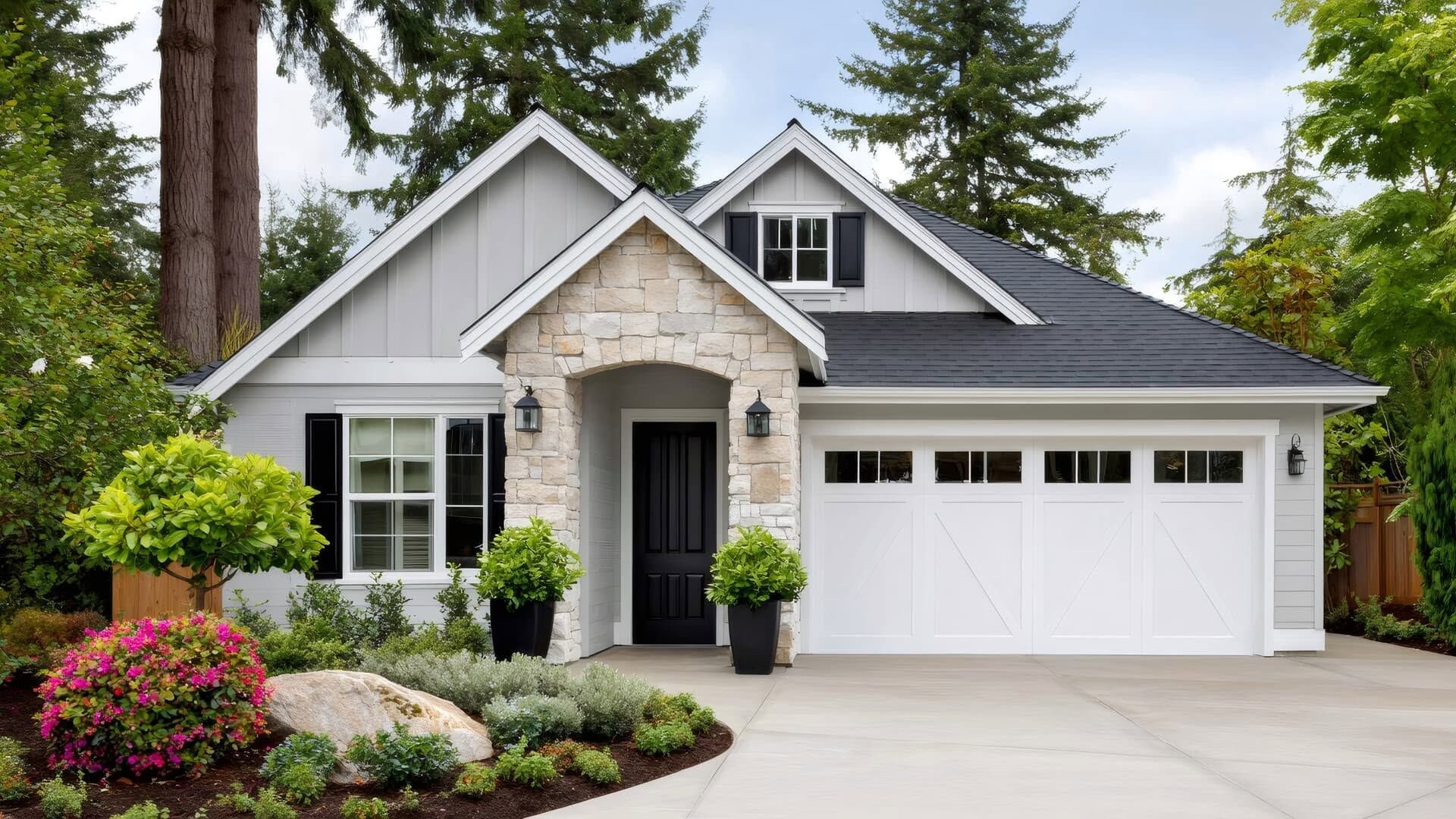 Single-story gray house with stone facade, white garage, and landscaped front yard amid tall trees