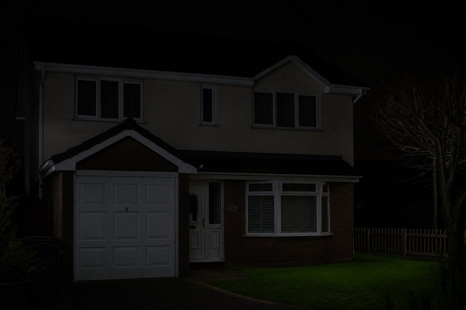 Dark two-story suburban house with attached garage and front porch at night