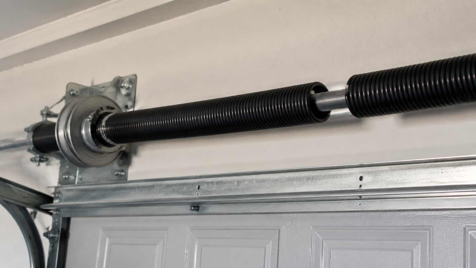 Garage ceiling with overhead door track, spring, and cables attached to a metal bracket.