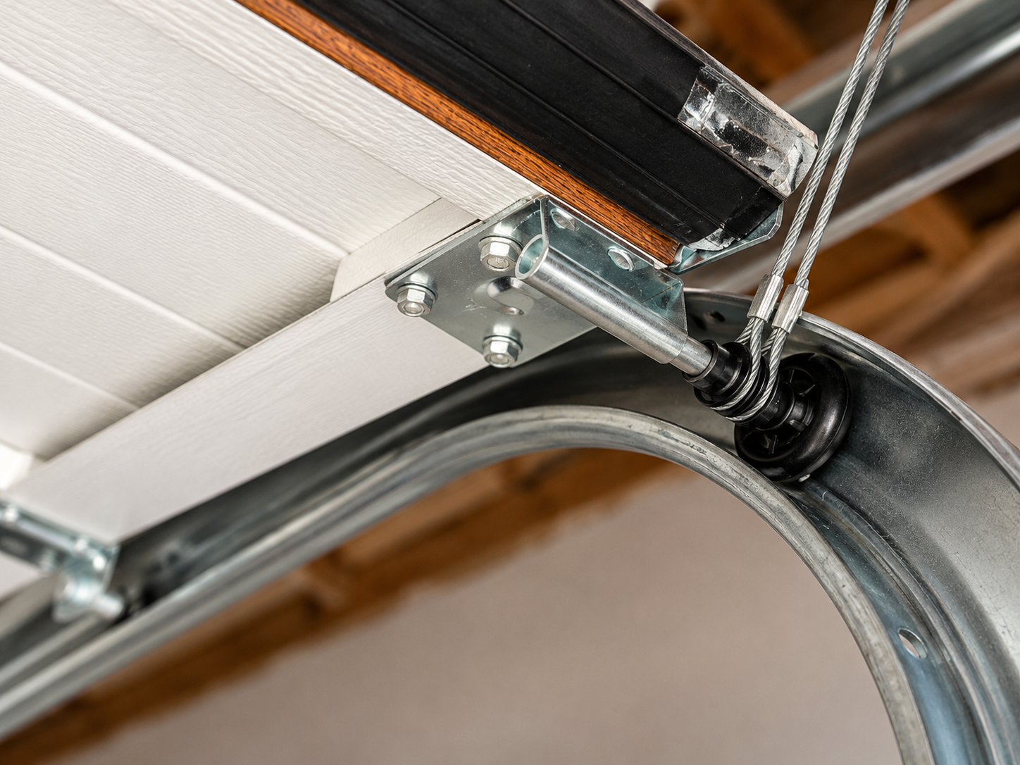 Close-up of a garage door track, hinge, and spring mechanism on a white overhead door.