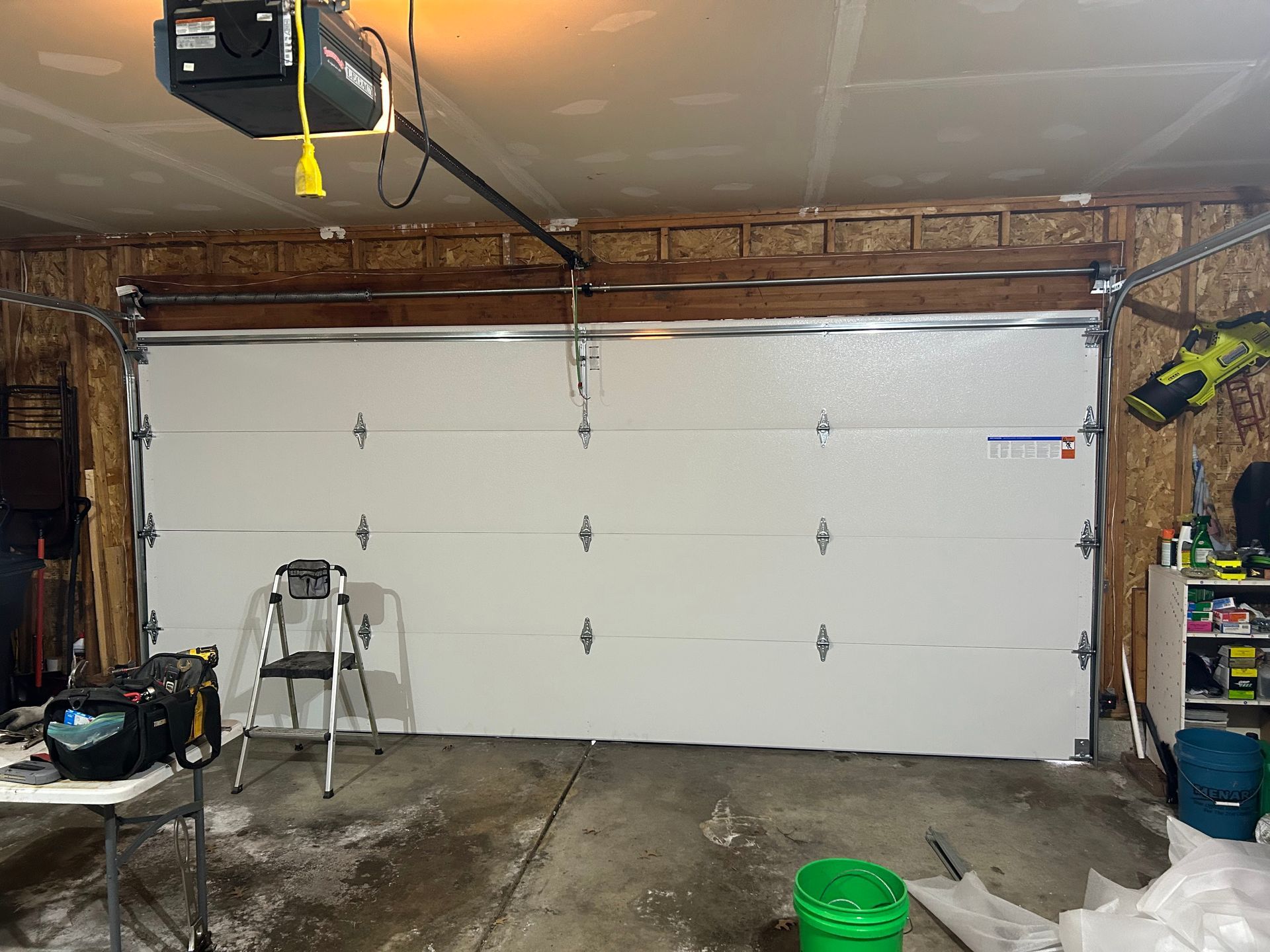 Single-car garage with a closed white sectional door, tools, and a wet concrete floor.