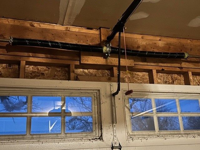 Garage door opener mounted on exposed beams above a white garage door with windows
