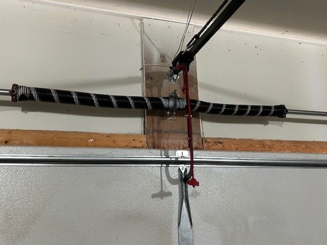 Garage door opener with a black wrapped beam, red clamp, and hanging cords against a white wall.