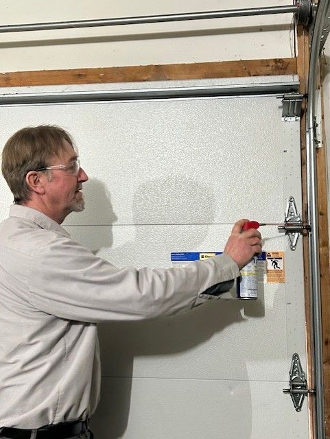 Man spraying lubricant on a garage door hinge with an aerosol can