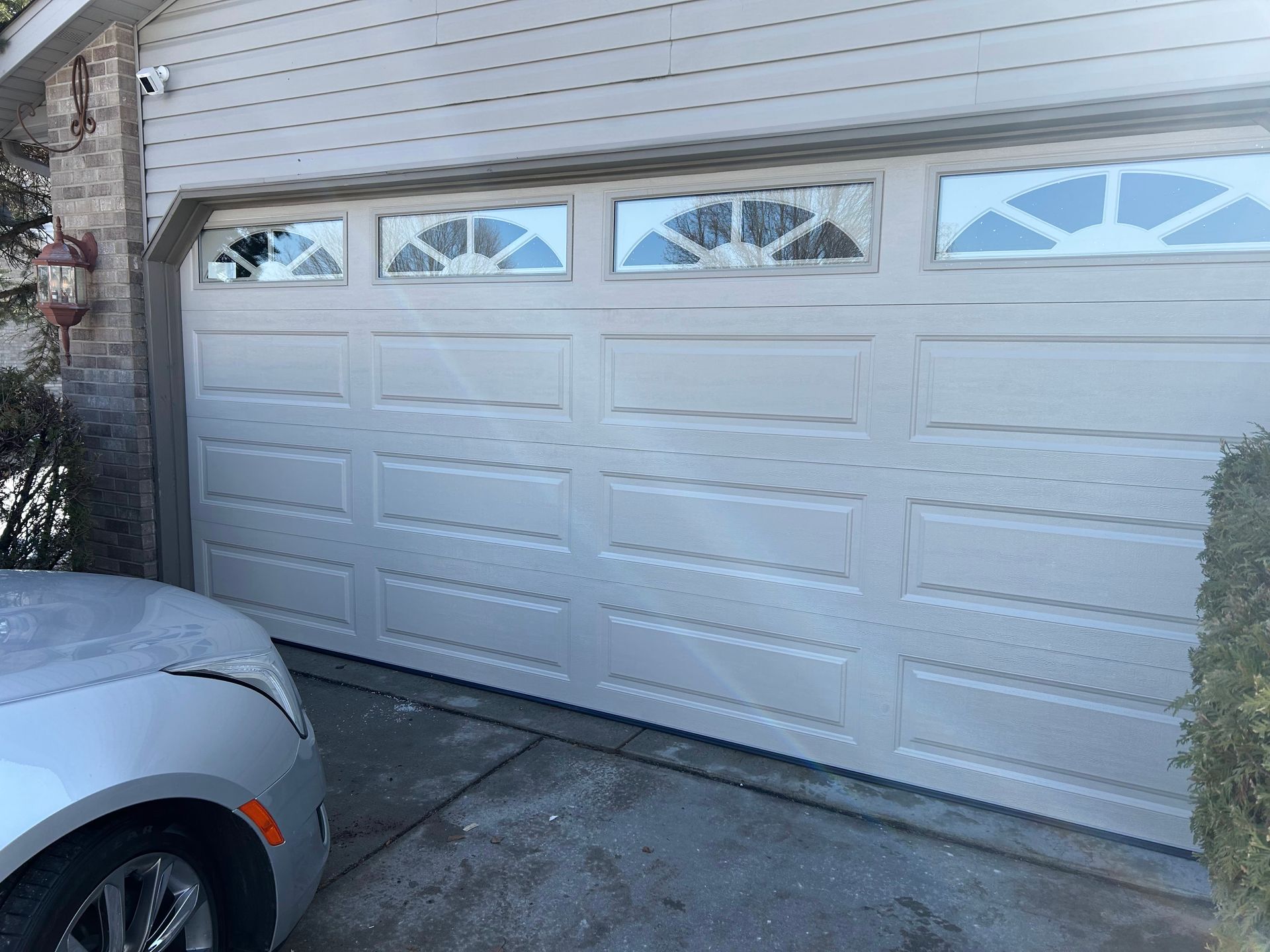 White garage door with four small window panels, viewed beside a parked silver car in a driveway