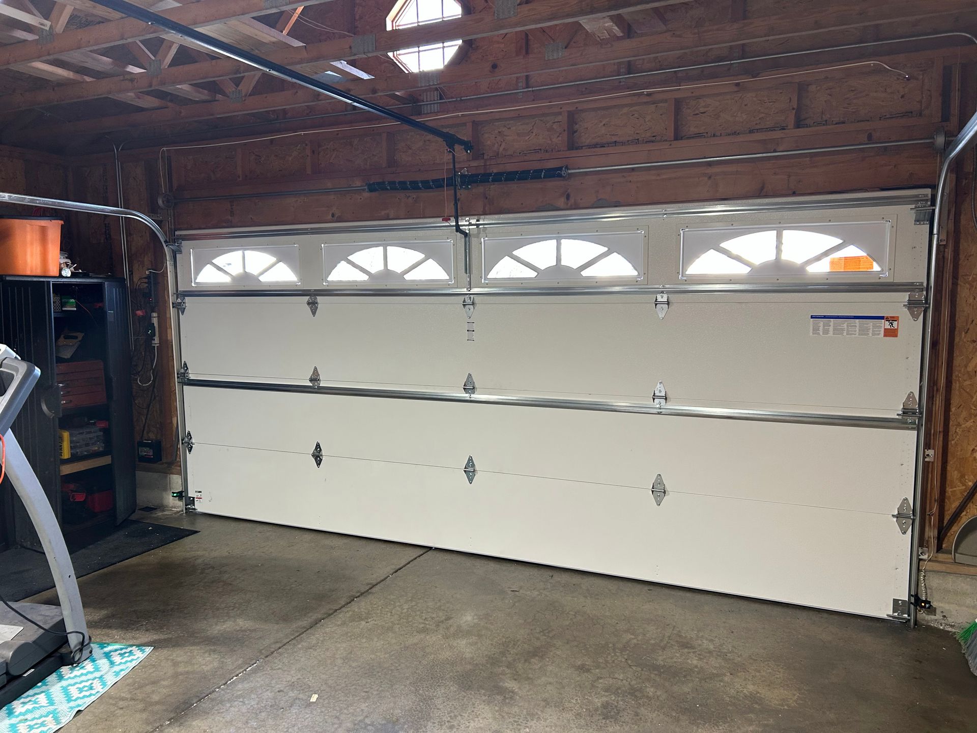 Interior of a garage with a closed white sectional door and exposed wooden ceiling beams