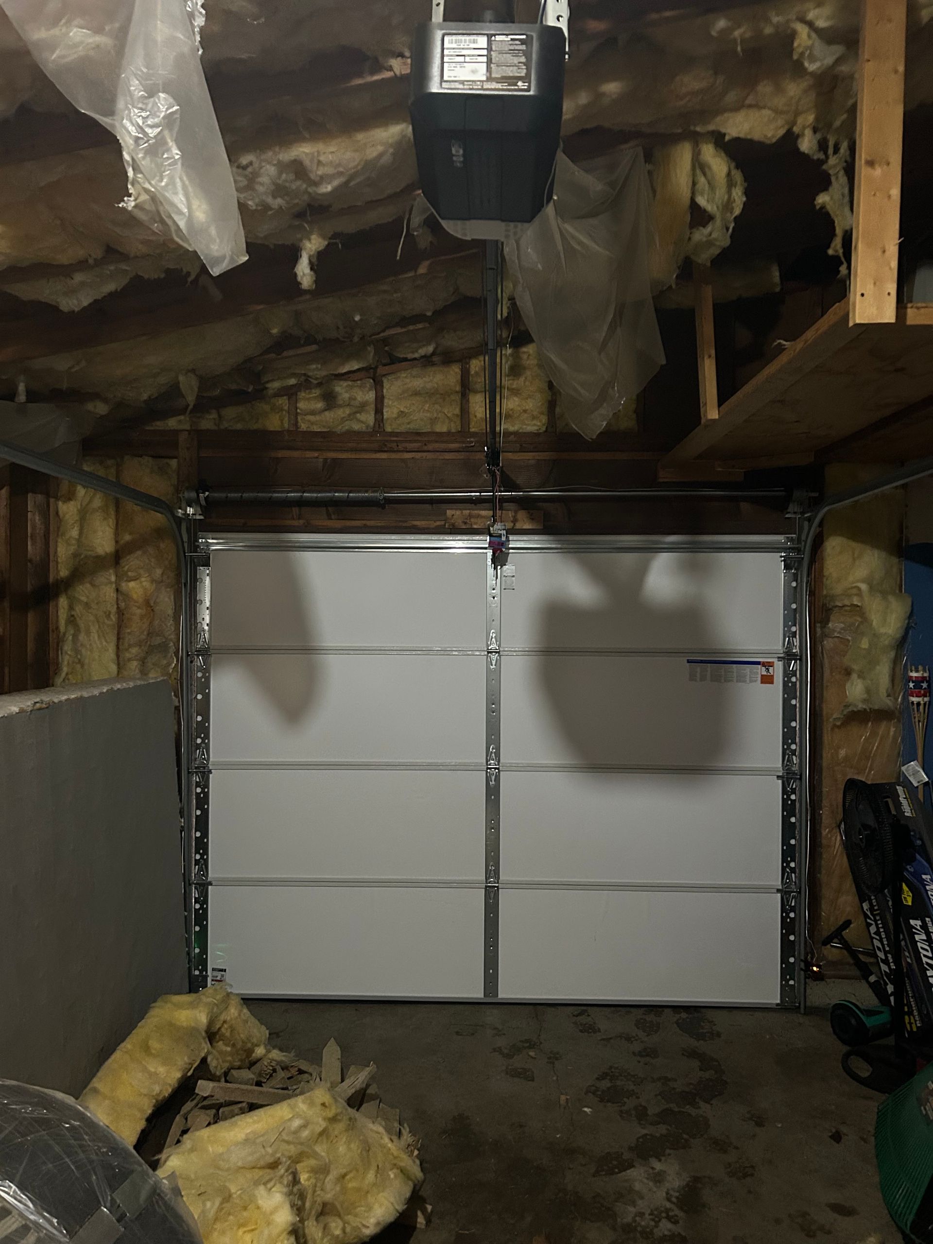 Closed white garage door in an unfinished basement with exposed insulation and a concrete floor