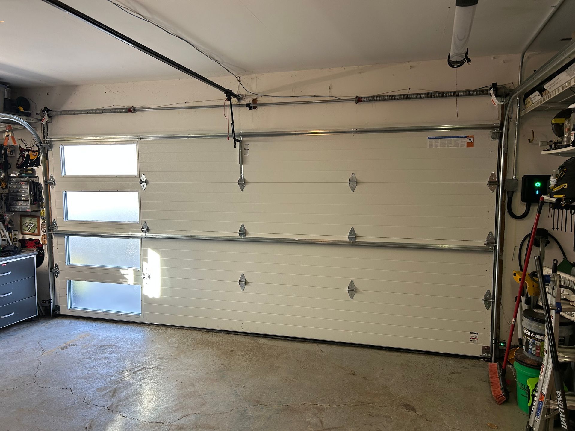 Empty garage interior with closed white sectional door, concrete floor, and wall-mounted tools on the right