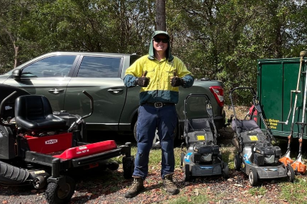 Mowbuddy Jack standing outside his trailer and gardening equipment.
