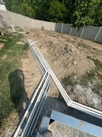 White pipes laid on ground in a construction site near a concrete fence and pile of dirt.