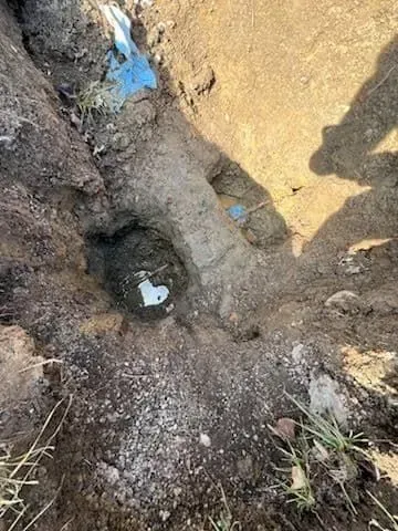 Worker digging a trench near a sidewalk, using a tool to bore under the grass.