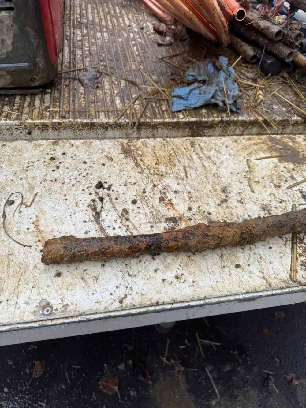 Rusty metal pipe on a dirty, white surface, with copper tubes in the background.