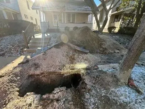 Large sinkhole in front yard of a house, with excavated dirt piled around it.