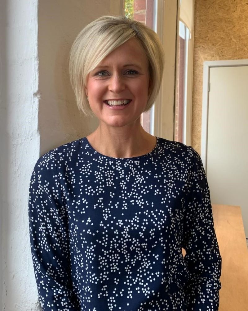 A woman wearing a blue shirt with white polka dots is smiling