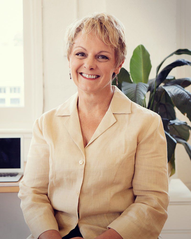 A woman in a tan jacket is smiling for the camera