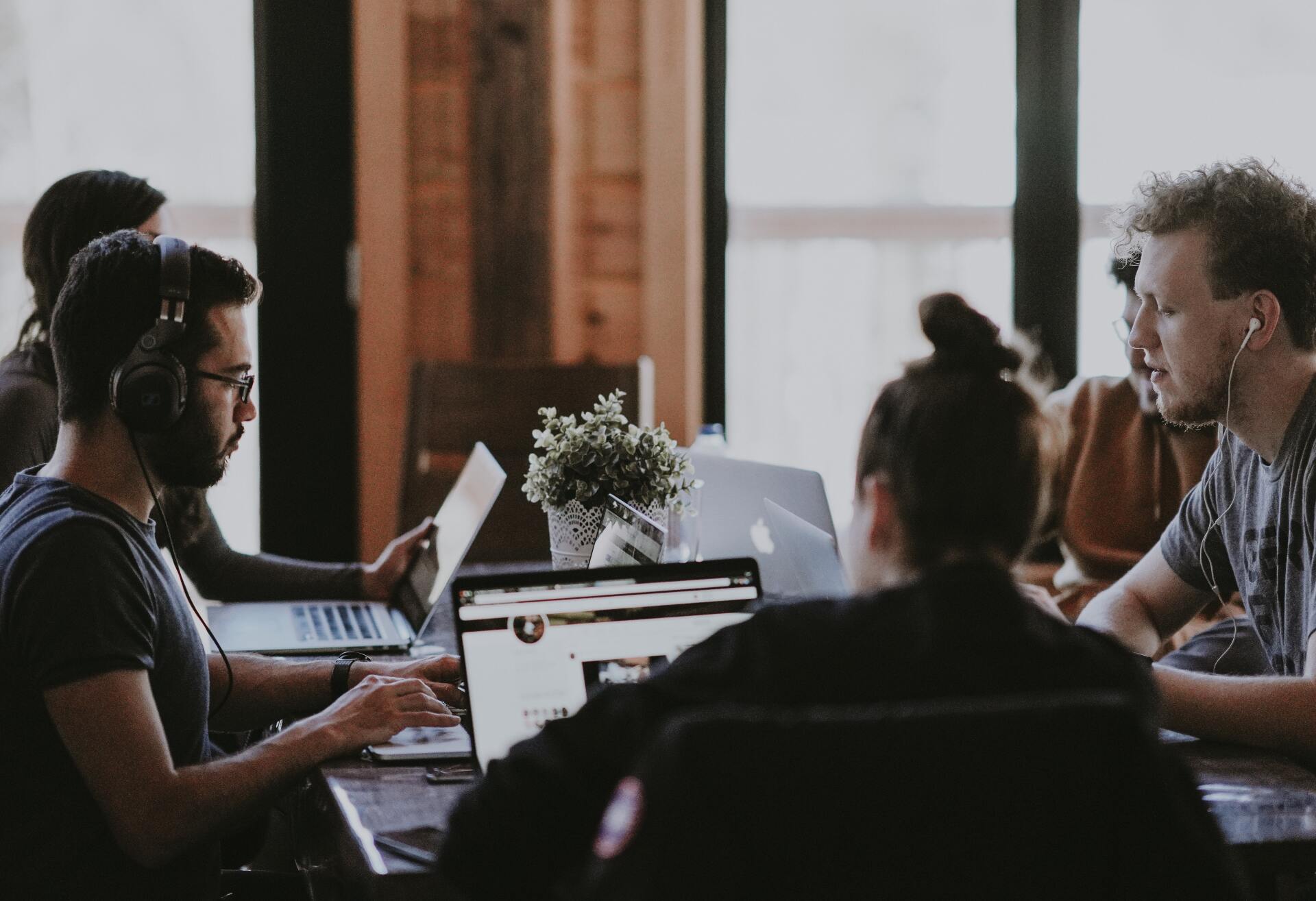 A group of people are sitting around a table with laptops.