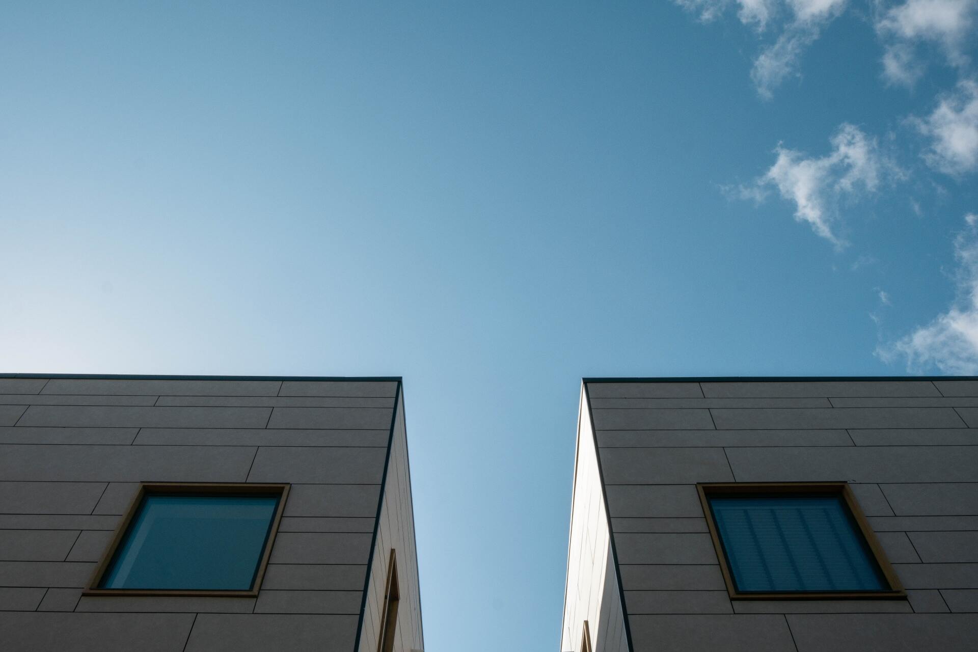 Looking up at two buildings with square windows against a blue sky.