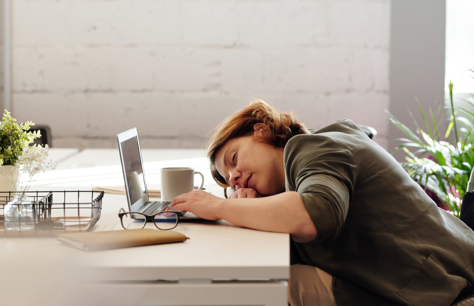 A woman is sleeping at a desk in front of a laptop computer.