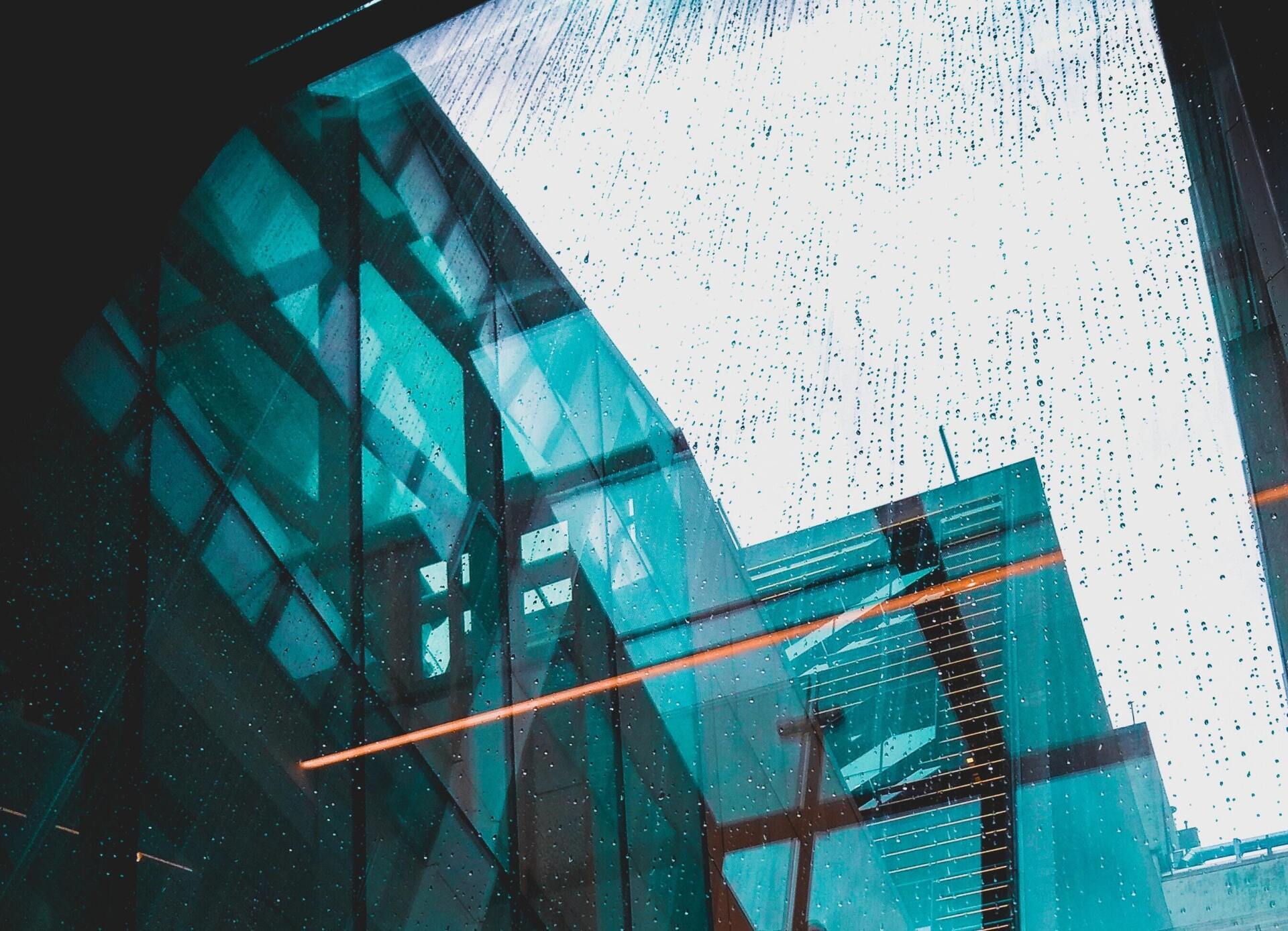 A reflection of a building in a window with rain drops on it.