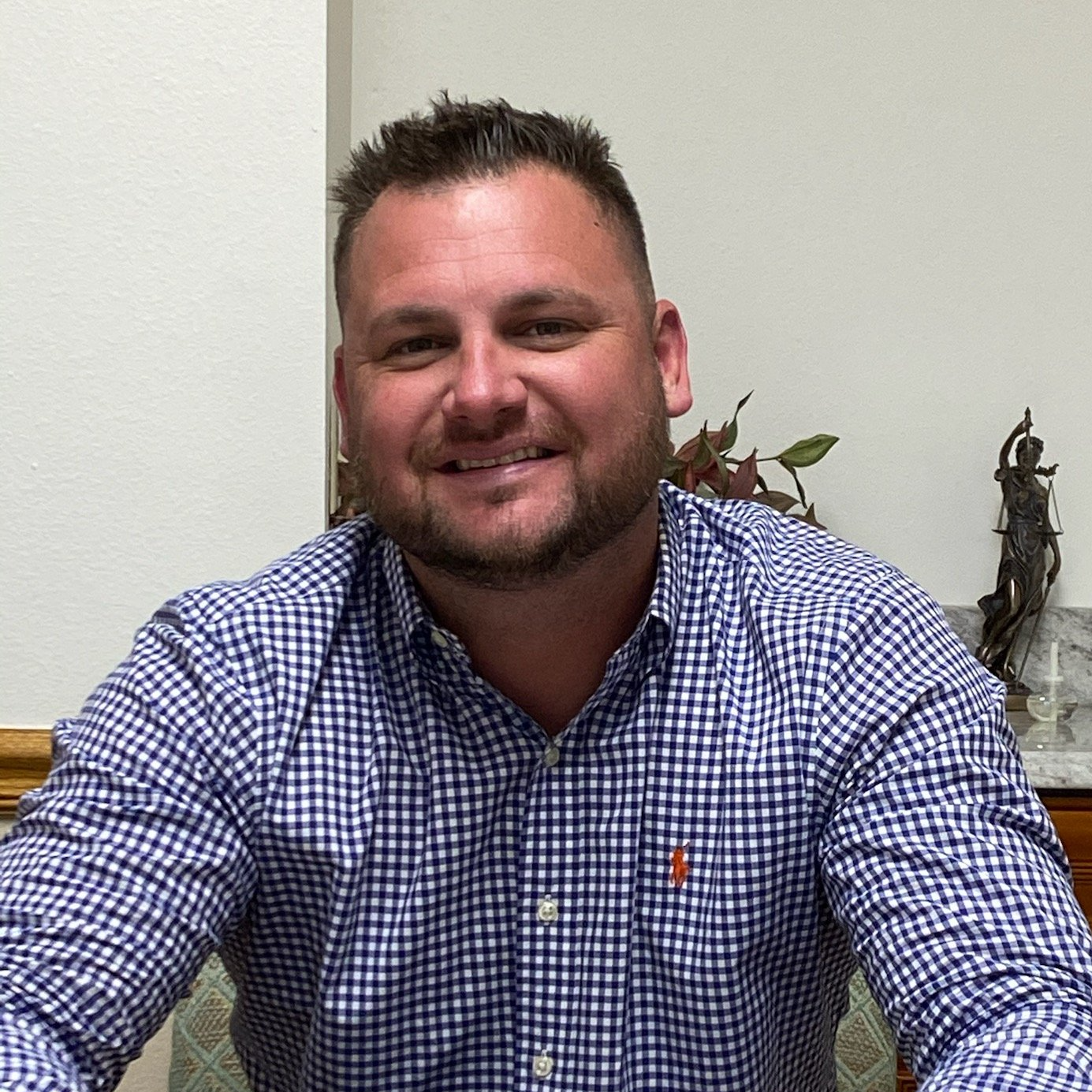 A man in a plaid shirt is smiling for the camera while sitting at a table.