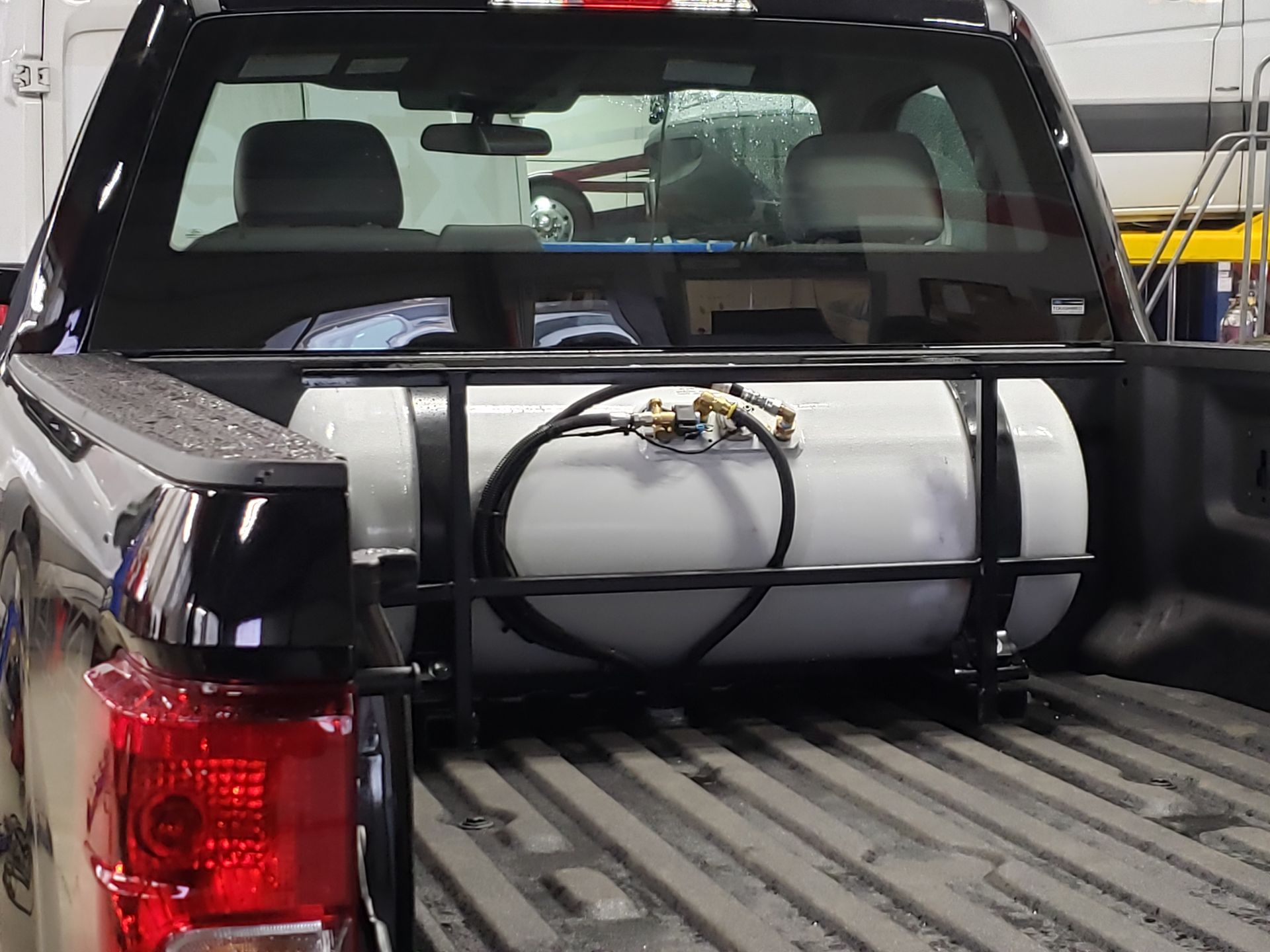 Truck bed with a white cylindrical tank secured by straps in the cargo area.