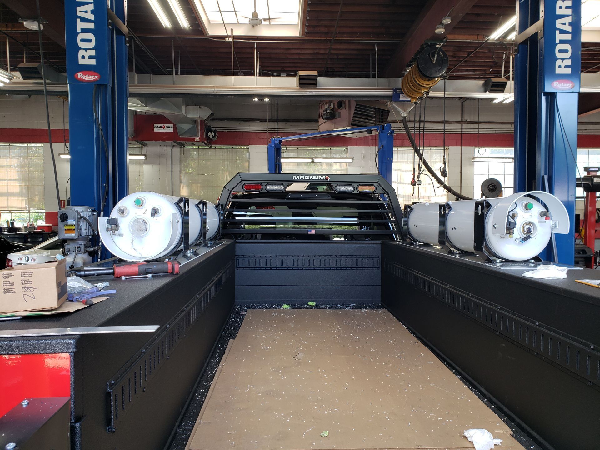 Car lift in an auto shop with a vehicle centered between two blue Rotary lift posts.