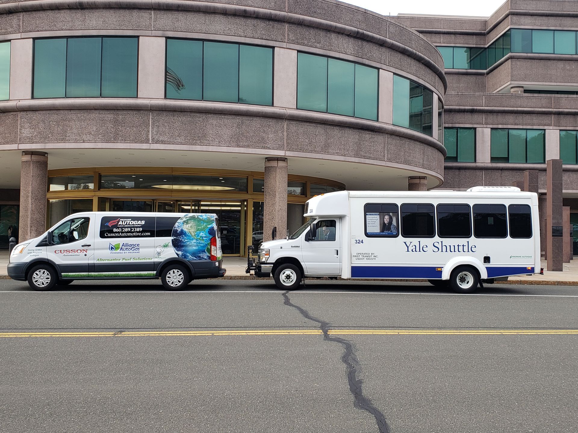 Two white shuttle vans parked outside a building with large green-tinted windows.